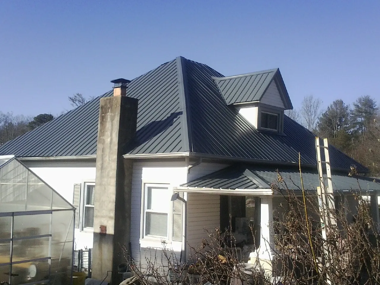 Dark blue standing seam metal roof on a white farmhouse with dormer — Slate & Tile Roof Repair by Roofing Brothers in Altus
