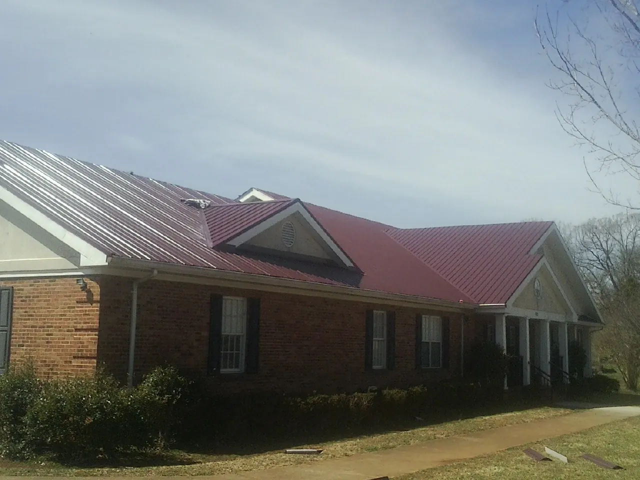 Red metal roof with gabled entries on a long brick building, from a Hail Damage Roof Repair job in Altus