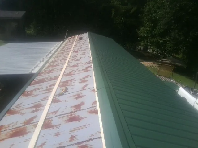 Old rusted panels beside newly installed green metal roofing — Wind Damage Roof Repair by Roofing Brothers in Altus