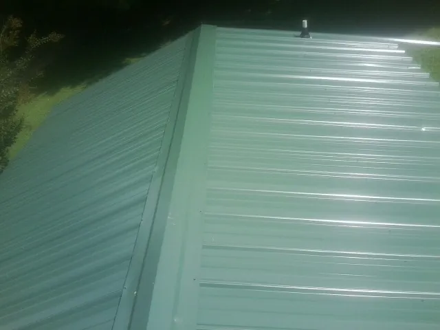 New green metal panels meeting at the ridge of a roof — Flat Roof Repair work by our crew in Altus