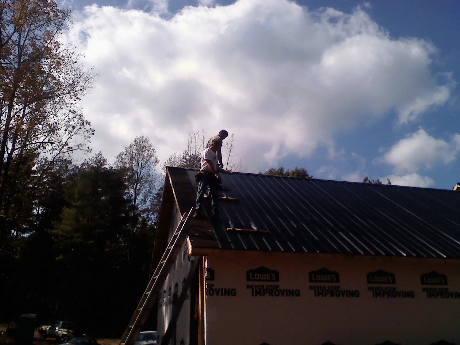 Roofer fastening dark metal panels high against a cloudy sky, from a Roof Inspection job in Altus