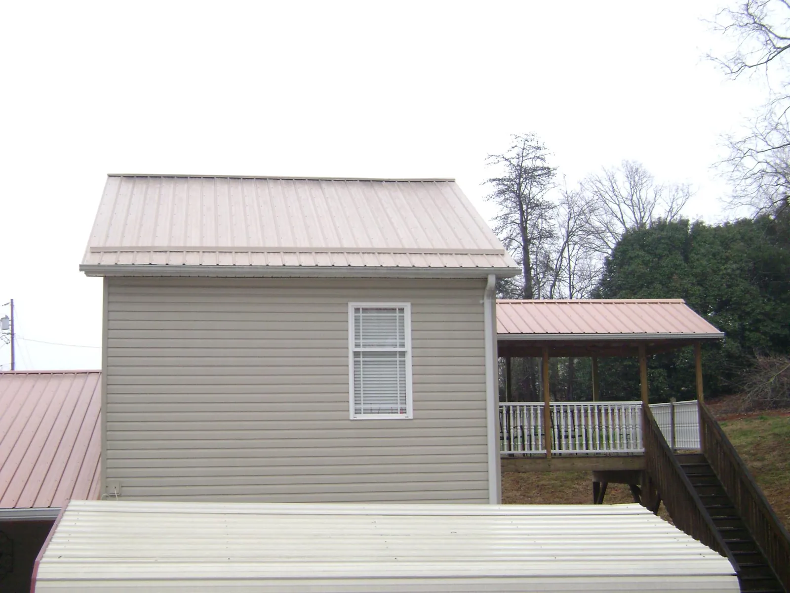 Tan metal roofs on a two story addition and attached porch, from a Roof Replacement job in Altus